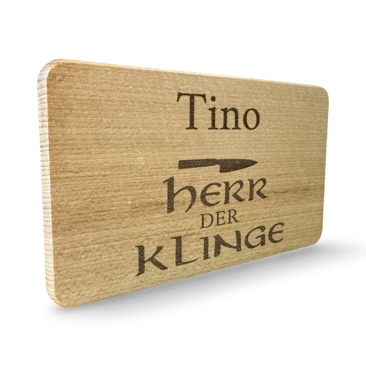 Schräge Ansicht eines personalisierbaren Frühstücksbrettes aus Holz mit Lasergravur „Tino – Herr der Klinge“ und Messer-Motiv