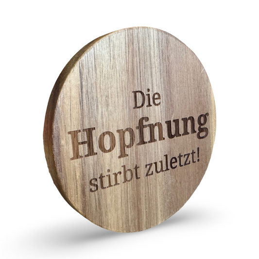 Schräge Ansicht eines Untersetzers aus Holz mit lasergraviertem Schriftzug „Die Hopfnung stirbt zuletzt“ – dekorativer Getränkeuntersetzer für Bierliebhaber