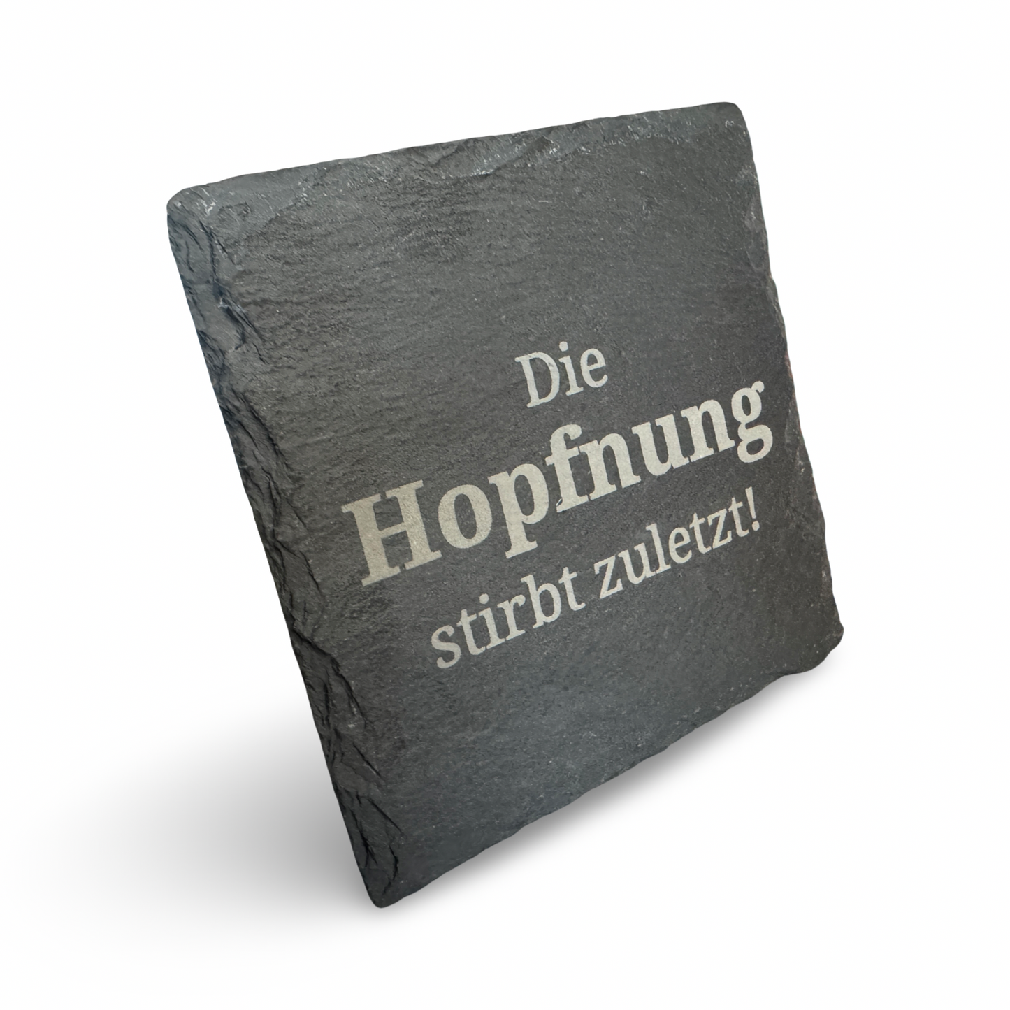 Schräge Ansicht eines Untersetzers aus Schiefer mit lasergraviertem Schriftzug „Die Hopfnung stirbt zuletzt"  – dekorativer Getränkeuntersetzer für Bierliebhaber
